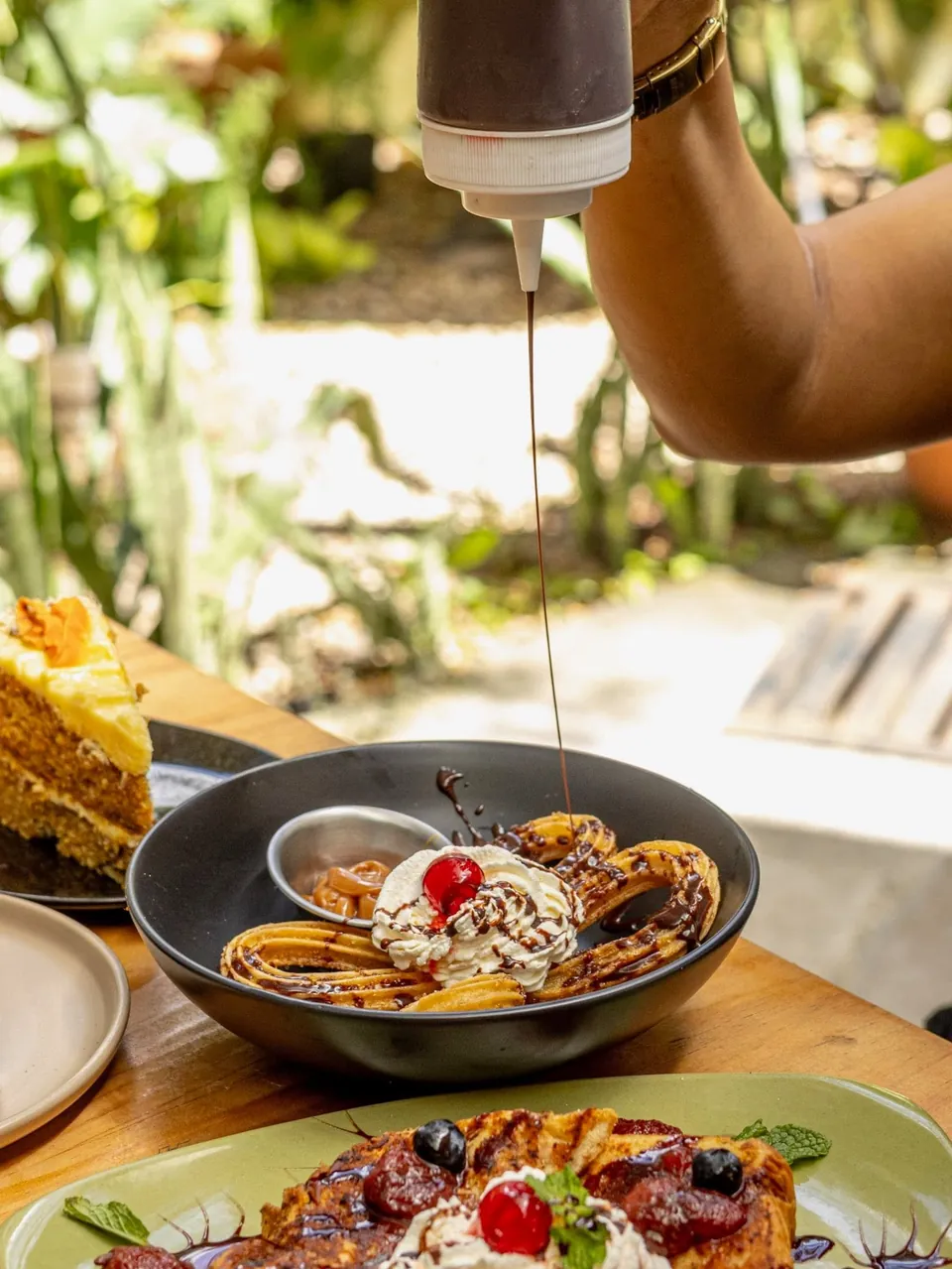 Chocolate caliente cae sobre un bol de churros, con el jardín desenfocado detrás
