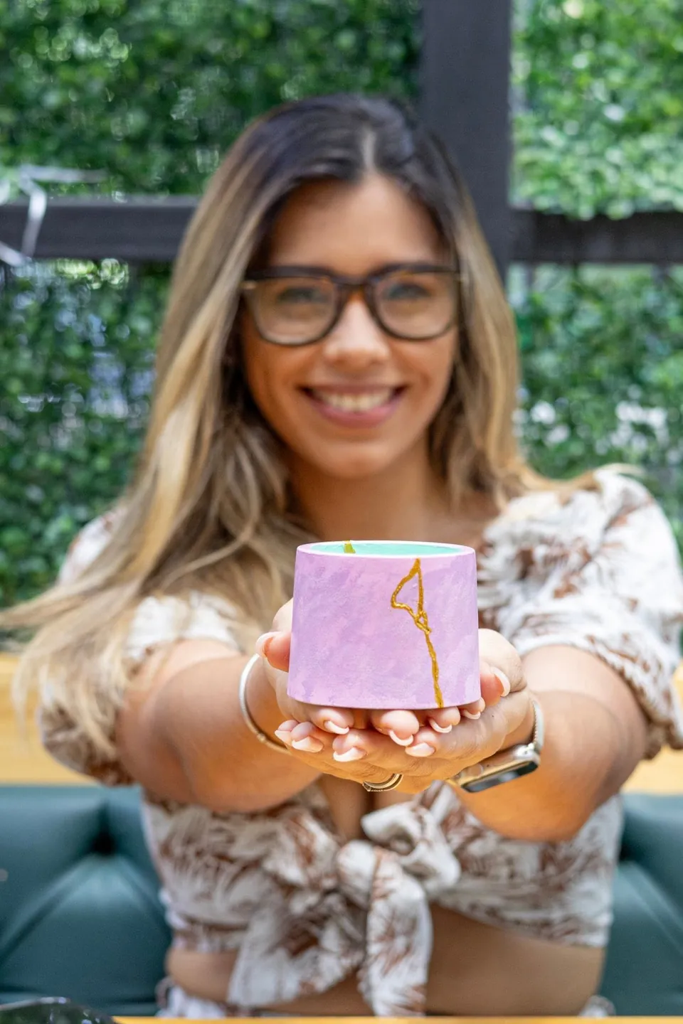 Una persona ofrece a la cámara una taza rosada reparada con líneas doradas, pintada a mano